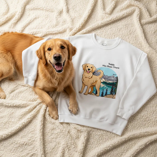 Personalized sweatshirt with a dog illustration, dog name, "Has Been There" badge, and Banff illustration, lying on a blanker with a Golden Retriever next to it. National Park Series.