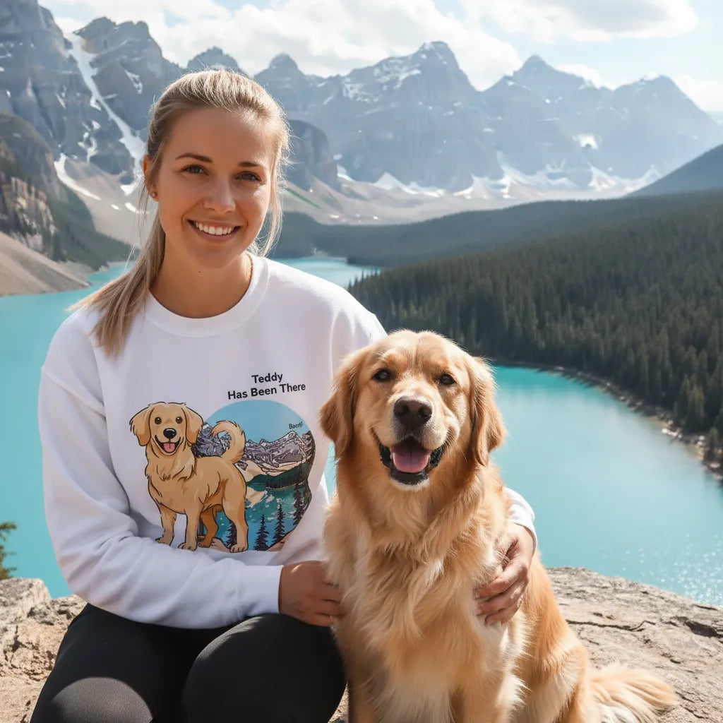 Female wearing a personalized sweatshirt with a dog illustration, dog name, "Has Been There" badge, and Banff illustration, sitting next to a Golden Retriever in front of the Moraine Lake. National Park Series.