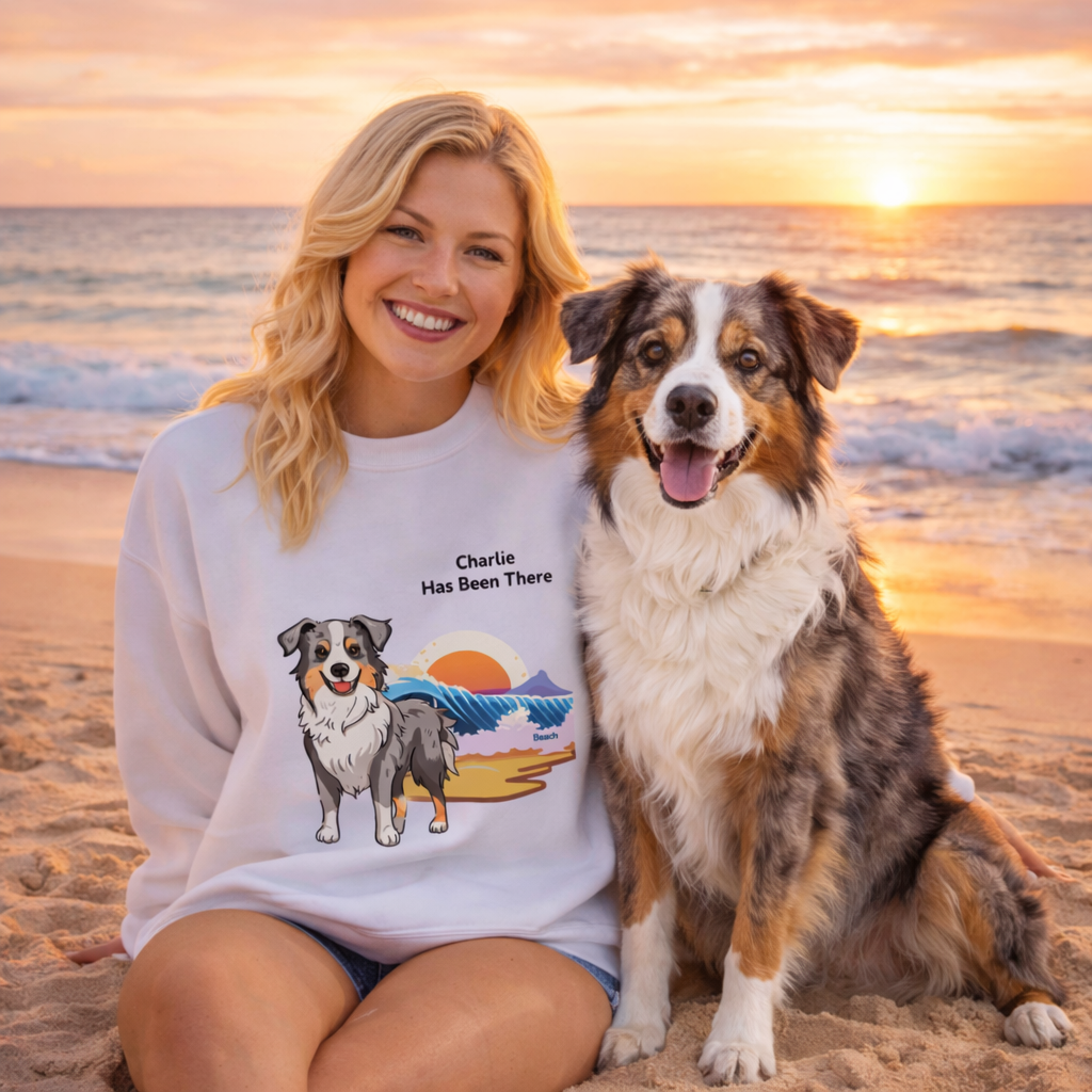 Female wearing a personalized sweatshirt with a dog illustration, dog name, "Has Been There" badge, and beach illustration, sitting next to an Australian Shepherd on a beach. Outdoor Adventure Series.