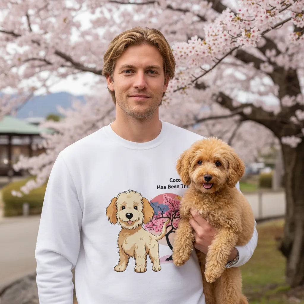 Male wearing a personalized sweatshirt with a dog illustration, dog name, "Has Been There" badge, and Japan illustration, holding a Poodle dog in front of cherry blossom. World Travel Series.
